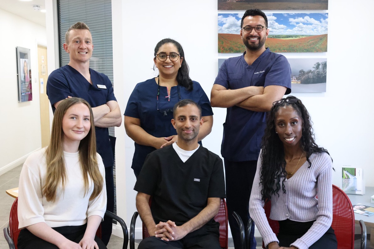 The Hitchin Dental Care clinical team in dark scrubs, standing and seated together in the practice
